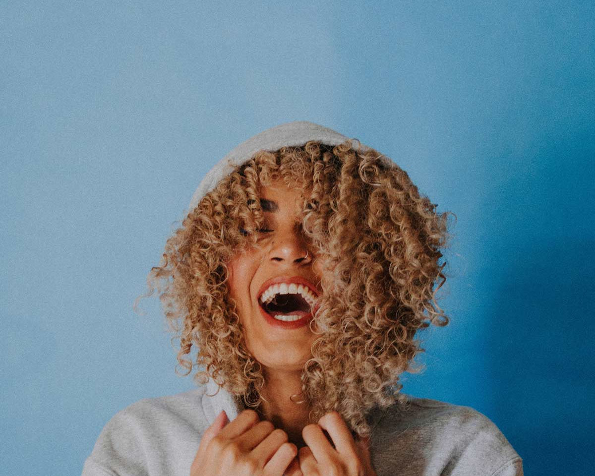 curly haired woman laughing wearing a hoodie
