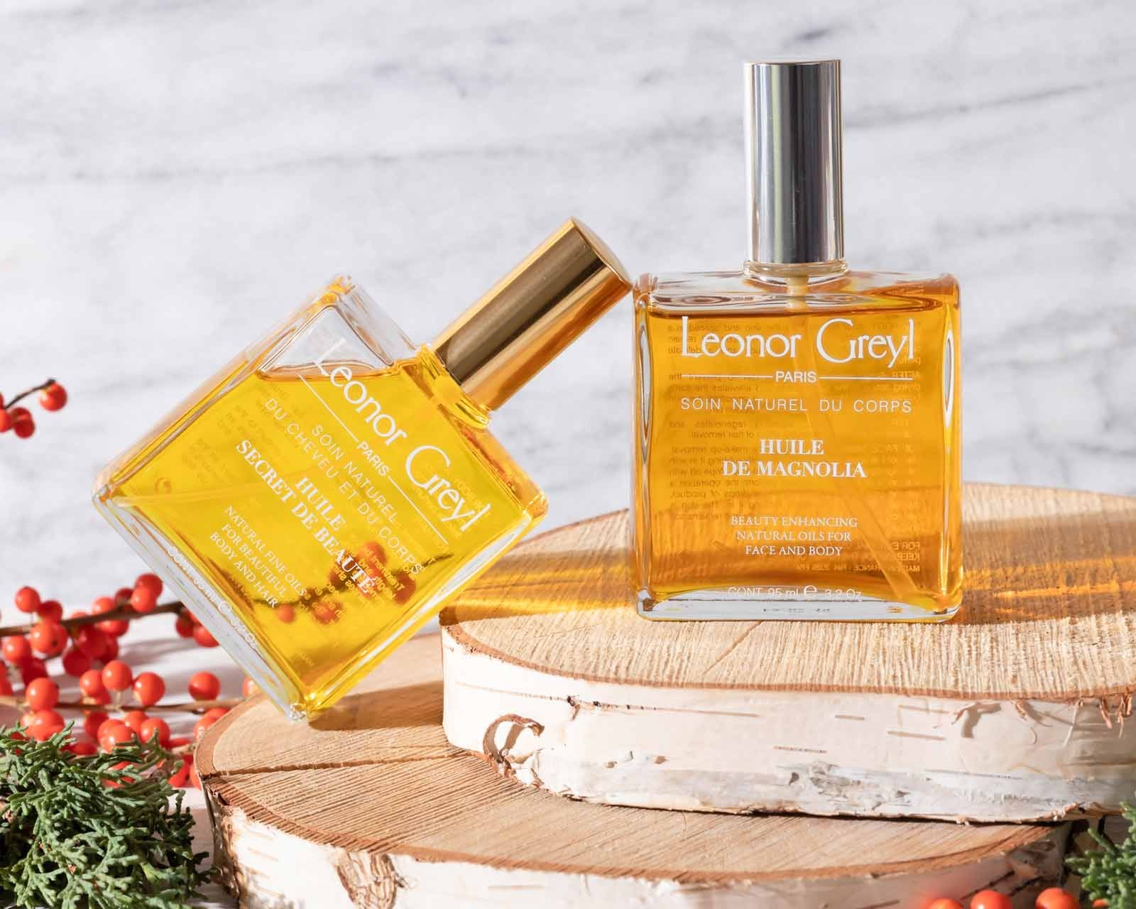 Two Leonor Greyl beauty oils on rustic wood trays with holly berries and greens