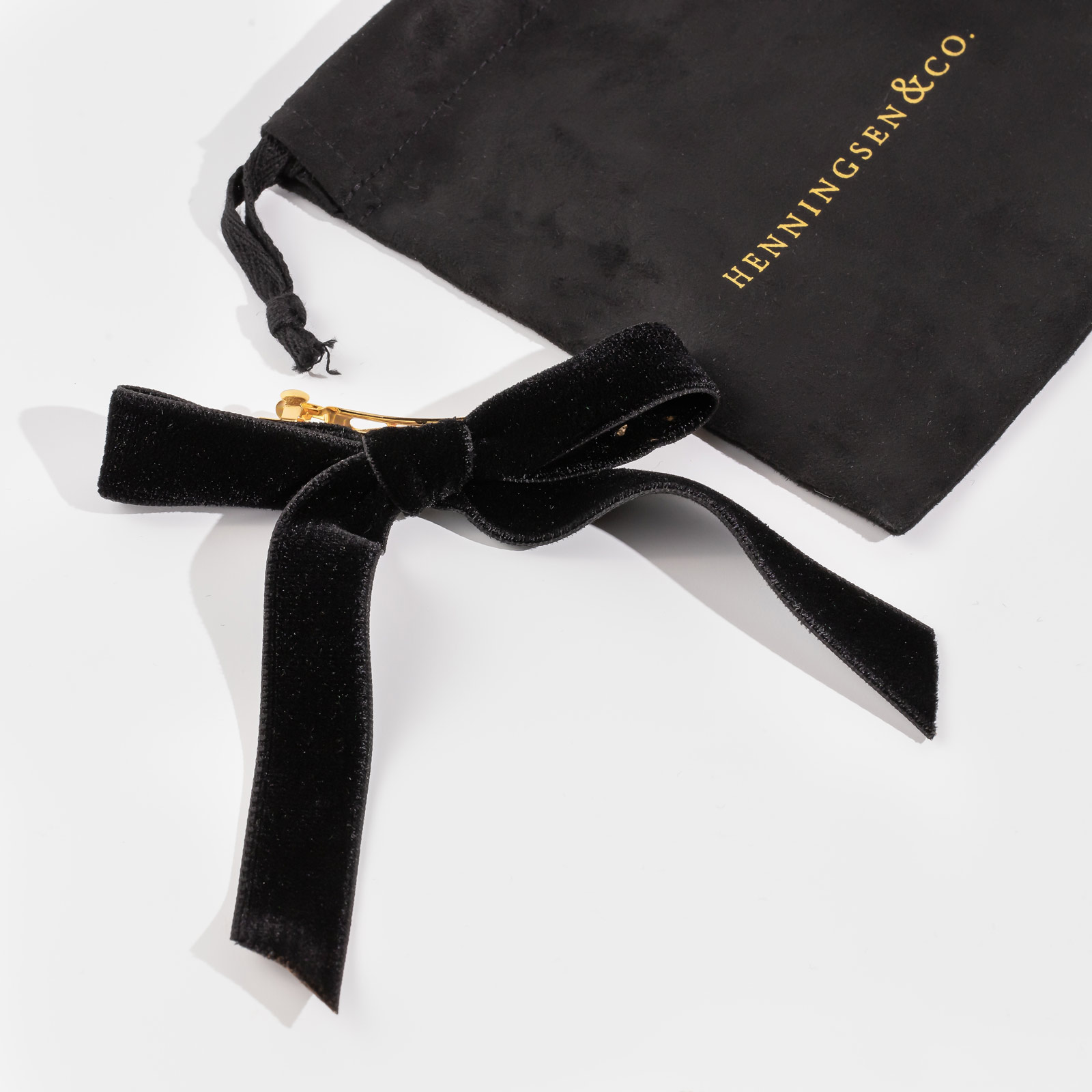 henningson and co black bardot bow and carrying bag on a white surface