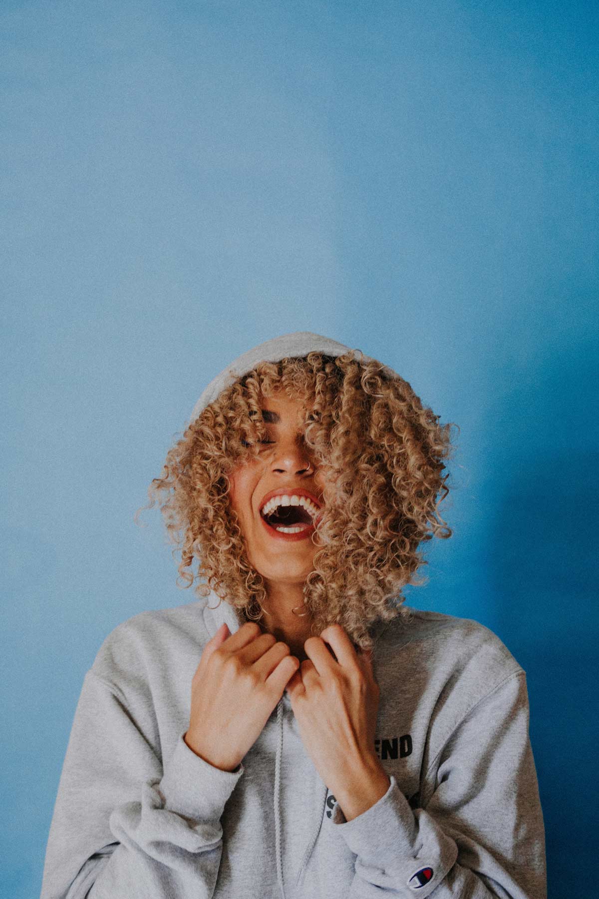 curly haired woman laughing wearing a hoodie