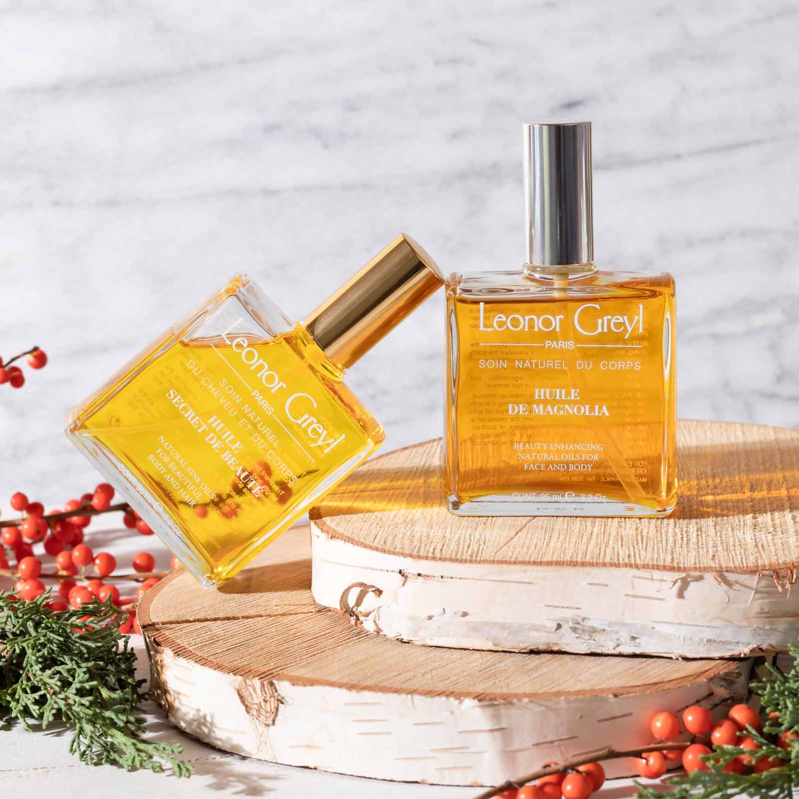 Two Leonor Greyl beauty oils on rustic wood trays with holly berries and greens