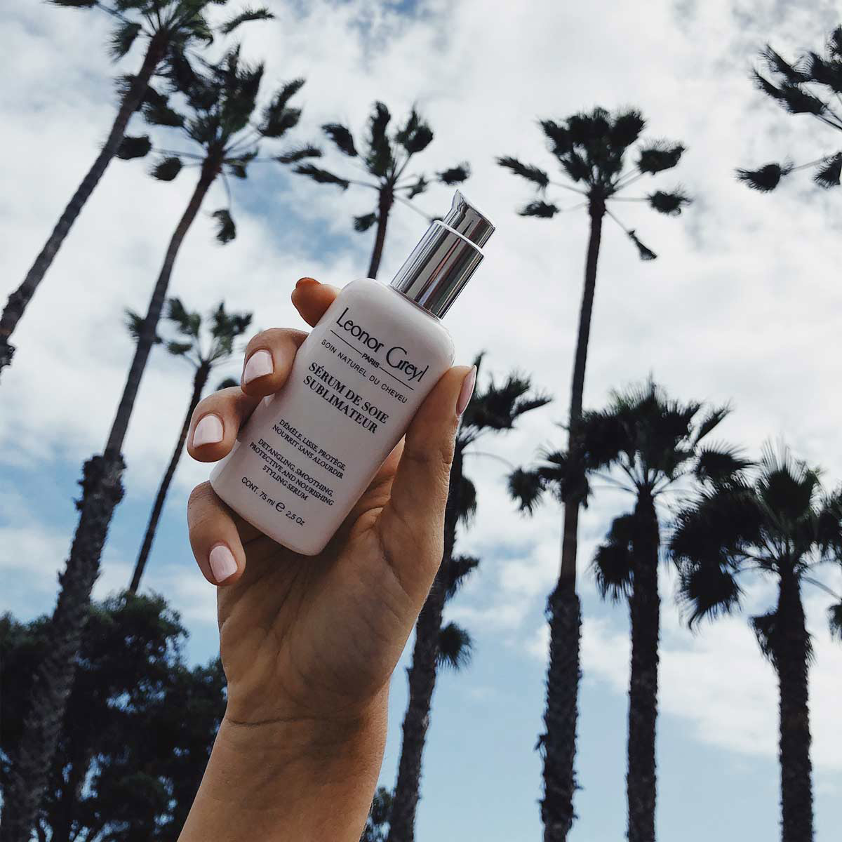 hand holding Leonor Greyl Serum with palm trees and sky in background